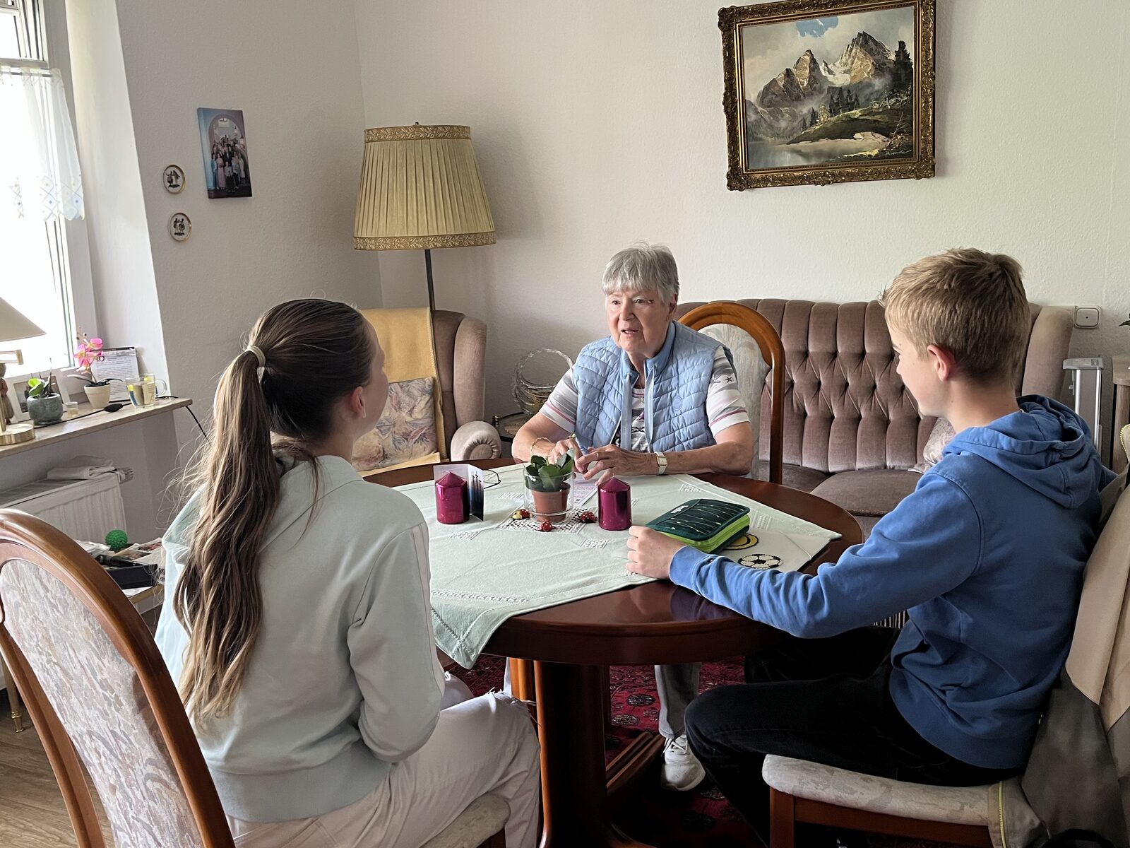 Eine Schülerin und ein Schüler des Domgymnasiums sitzen mit einer Bewohnerin des Mediana Wohnstifts in Fulda am Wohnzimmertisch und sprechen über Musik
